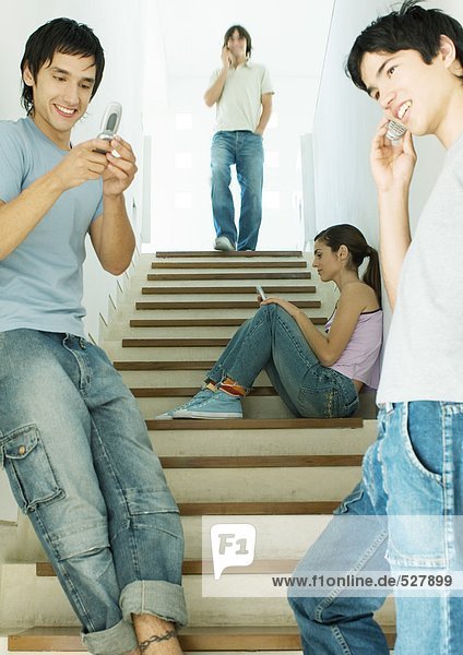 Vier junge Erwachsene  die jeweils ein Handy im Treppenhaus benutzen.