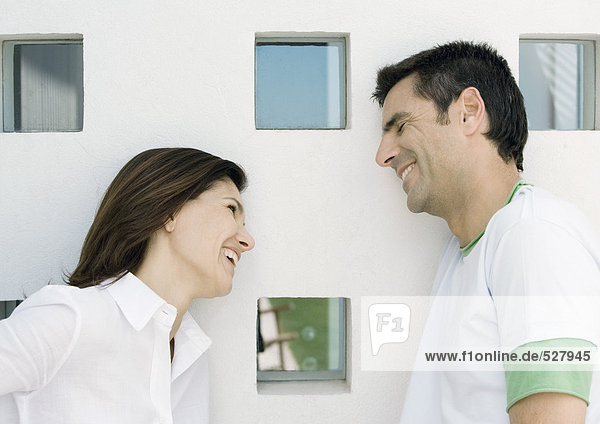 Woman and husband  both leaning against wall with squared windows and smilling