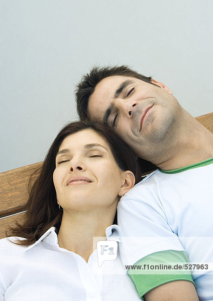 Couple resting on a bench  reclining with eyes closed and heads together  smiling  portrait