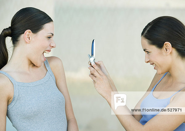 Junge Frau fotografiert einen Freund mit Handy  beide lachend