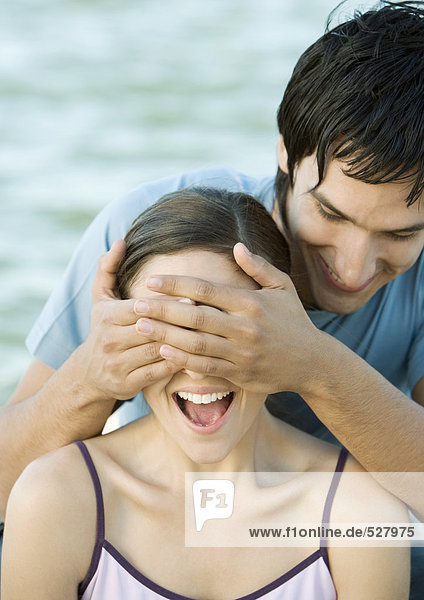 Young man covering his girlfriend's eyes  both laughing  portrait  close-up