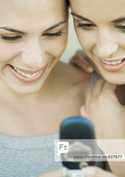 Two young women side by side looking down at a cell phone  both smiling  extreme close-up