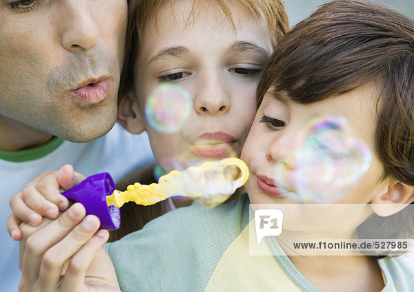 Vater hat Spaß mit seinen beiden Kindern  bläst Seifenblasen zusammen  Porträt  extreme Nahaufnahme