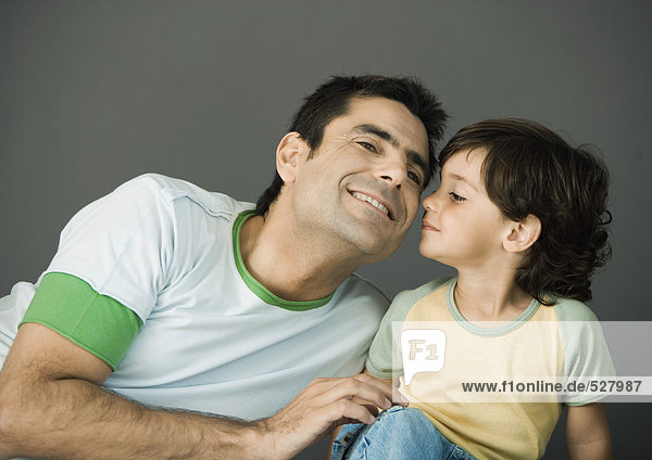Vater und Sohn sitzen Seite an Seite  Kind küsst die Wange seines Vaters  lächelnd  Porträt