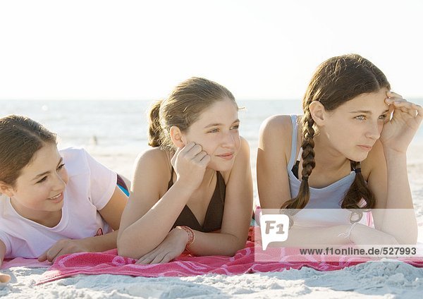 Three preteen girls lying on beach