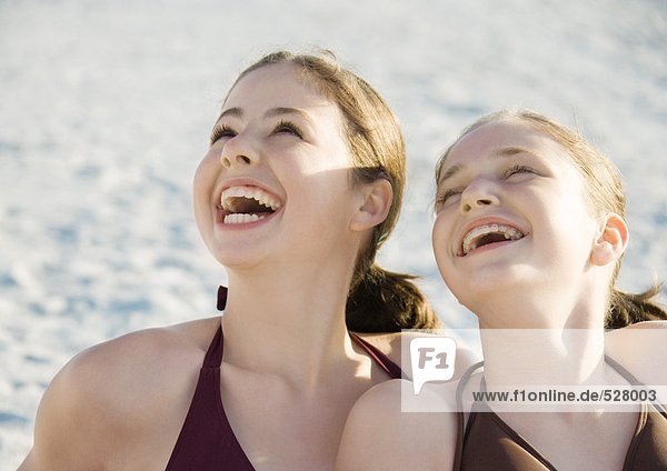 Zwei Mädchen  die am Strand lachen und aufschauen.