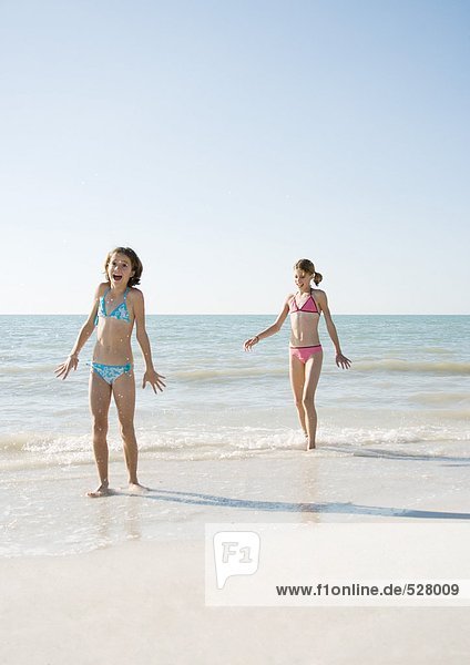 Two girls walking on beach  one with mouth open in surprise
