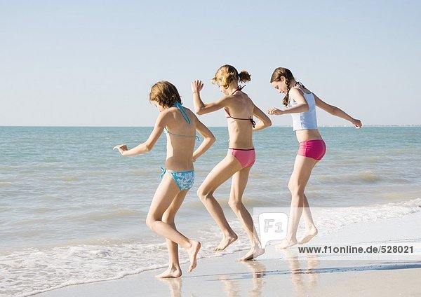 Three girls running toward water on beach