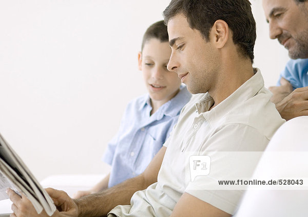 Man looking at newspaper with son and father