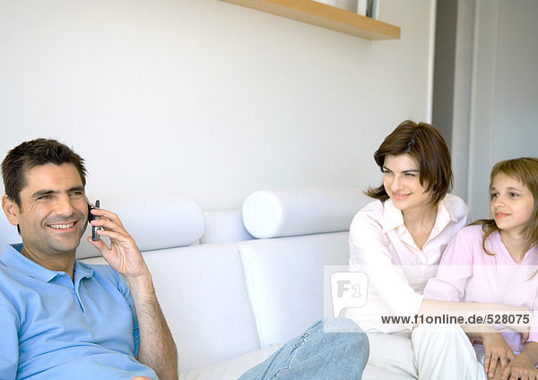 Man using cell phone while wife and daughter watch