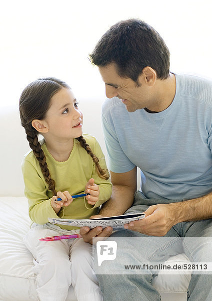 Vater und Tochter schauen sich gemeinsam das Malbuch an