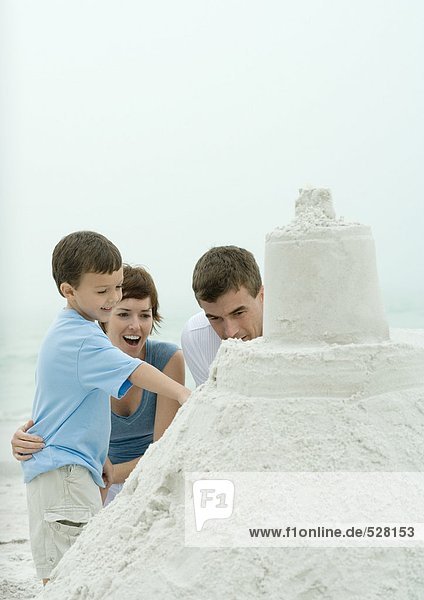Boy showing parents sand castle