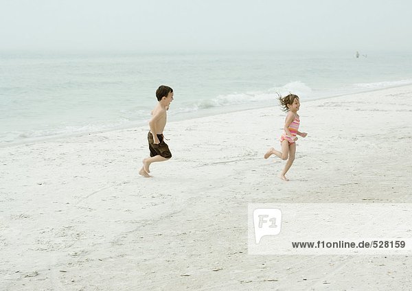 Junge und Mädchen  die am Strand rennen