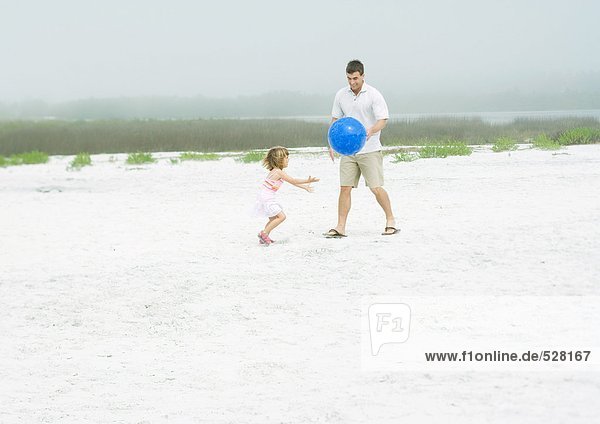 Mann spielt Ball mit Tochter auf Sand