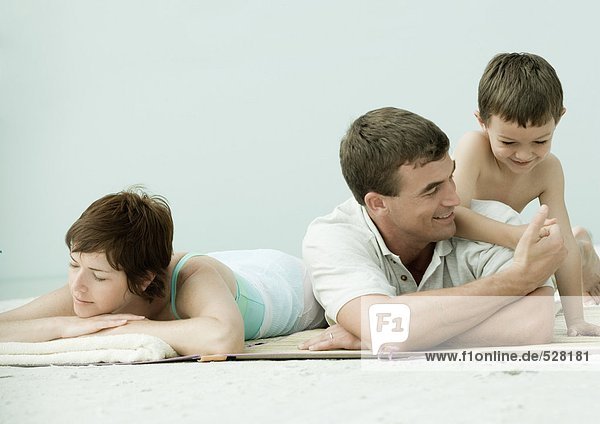 Familie liegt am Strand  Mann und Sohn ringen mit dem Daumen  während die Mutter schläft.