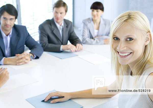 Businesswoman smiling at camera  meeting in background  portrait