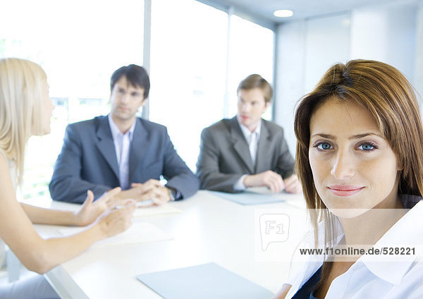 Businesswoman smiling at camera  meeting in background  portrait