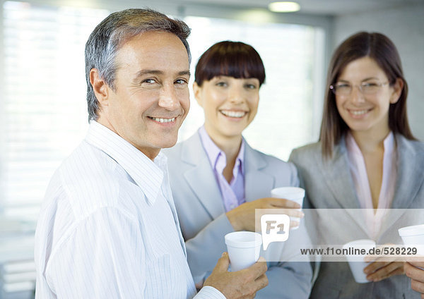 Business colleagues standing in office with cups in hands  smiling at camera