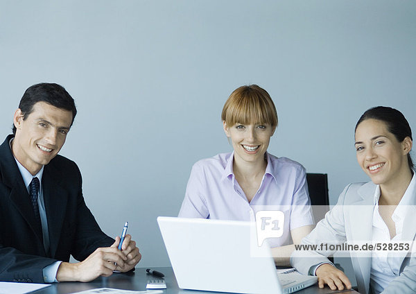 Business colleagues gathered around laptop  smiling