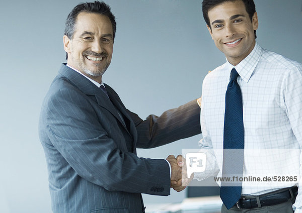 Business executives shaking hands  smiling at camera