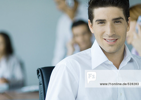 Businessman smiling at camera  colleagues in background  portrait