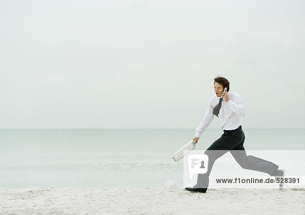 Businessman running on beach  with cell phone and briefcase