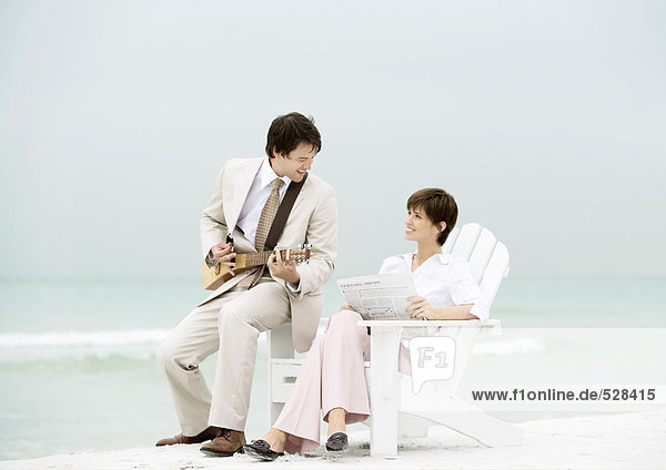 Geschäftsmann spielt Streichinstrument für Frau am Strand