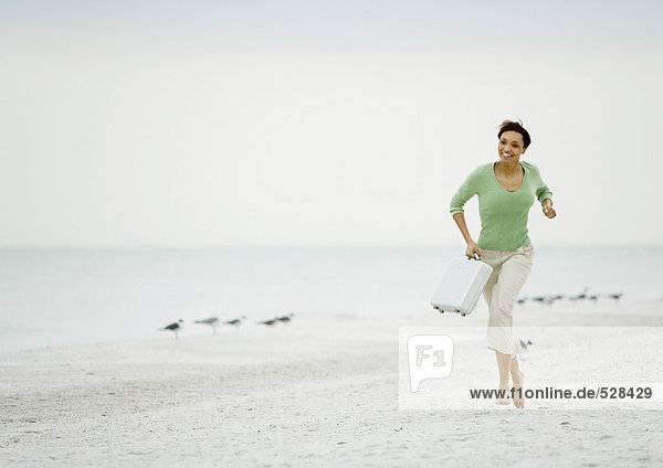 Frau läuft am Strand mit Aktentasche