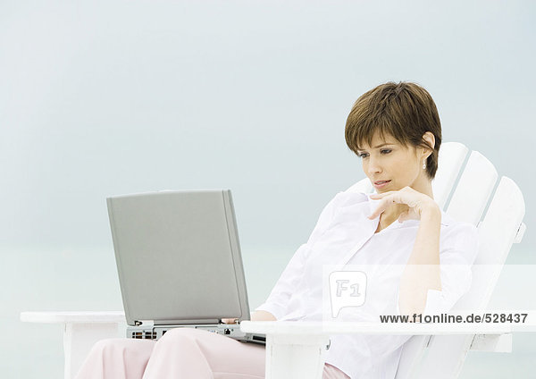 Woman sitting in deckchair using laptop
