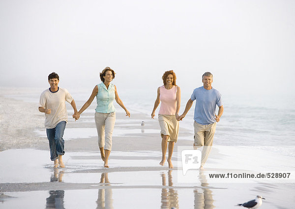 Two mature couples walking on beach  holding hands
