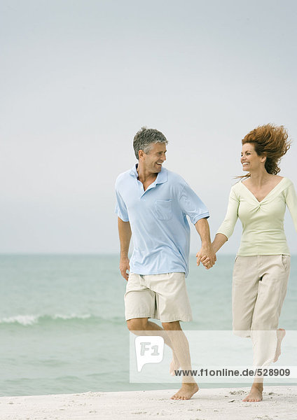 Ein reifes Paar  das Hand in Hand am Strand läuft.