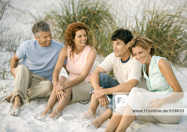 Two mature couples sitting in sand