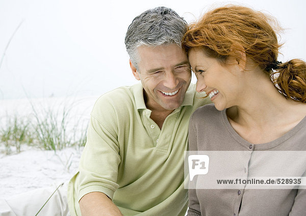 Mature couple sitting on beach  smiling with heads together