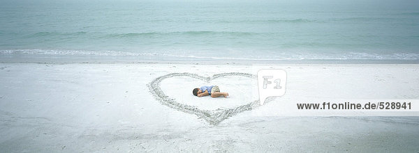 Child lying inside heart drawn on beach