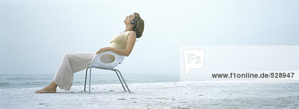 Frau sitzt im Sessel am Strand  trägt Kopfhörer