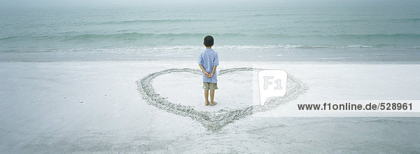 Boy standing inside heart drawn on beach  rear view