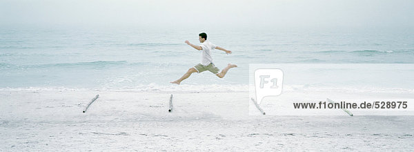 Mann läuft und springt über Baumstämme am Strand