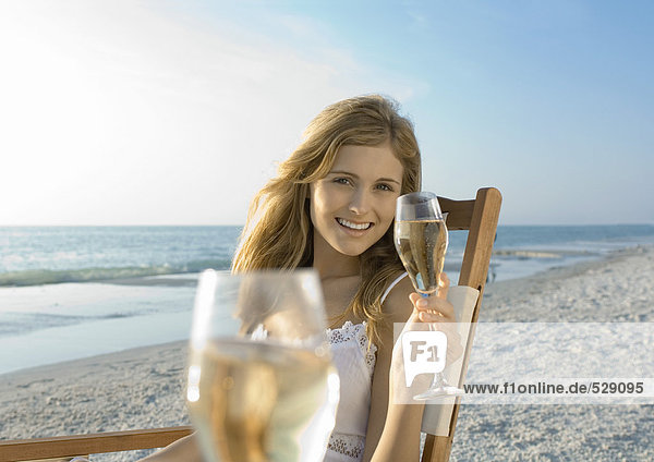 Junge Frau trinkt Champagner am Strand