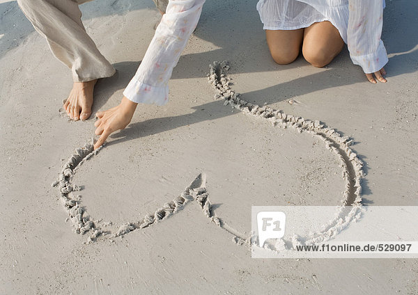 Woman drawing heart in sand on beach  partial view