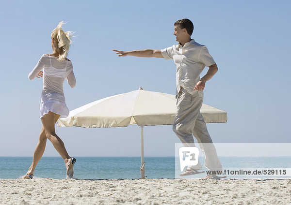 Ein Paar jagt sich gegenseitig um den Sonnenschirm am Strand.