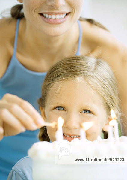Mutter entzündet Kerzen auf Geburtstagskuchen für Mädchen