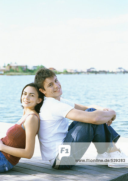 Young couple sitting back to back on dock