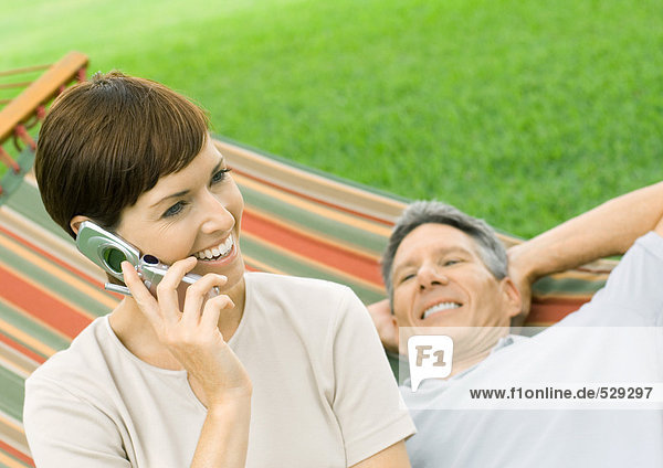 Woman using cell phone while man lounges on hammock