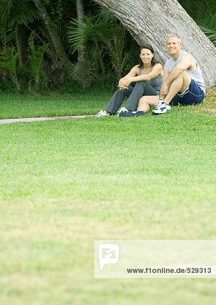 Paar in Trainingskleidung neben dem Baum sitzend