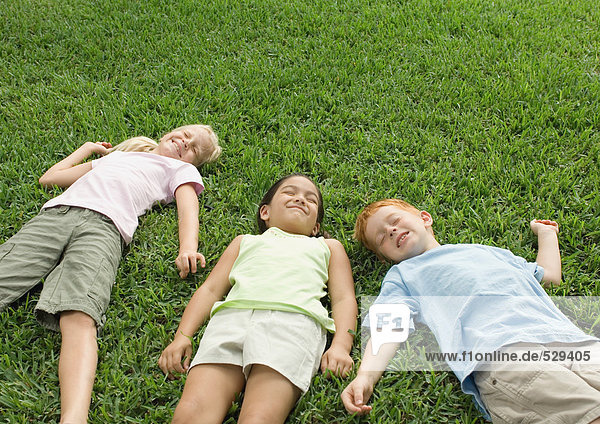 Drei Kinder im Gras liegend