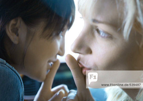 Zwei junge Frauen halten die Finger an die Lippen  den Mund.