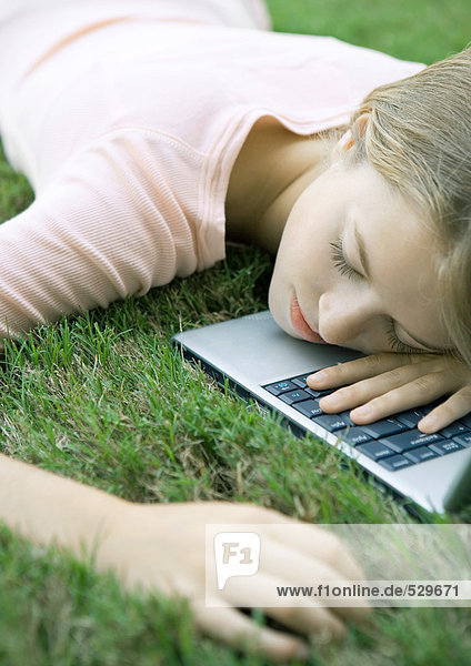 Teenager Mädchen im Gras  liegend mit Kopf auf Laptop-Computer