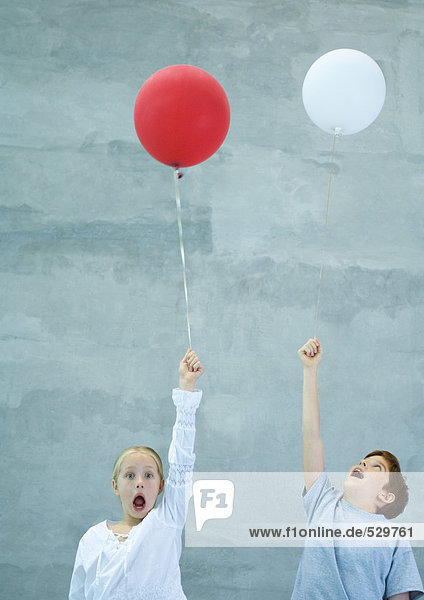 Zwei Kinder halten Luftballons und schreien