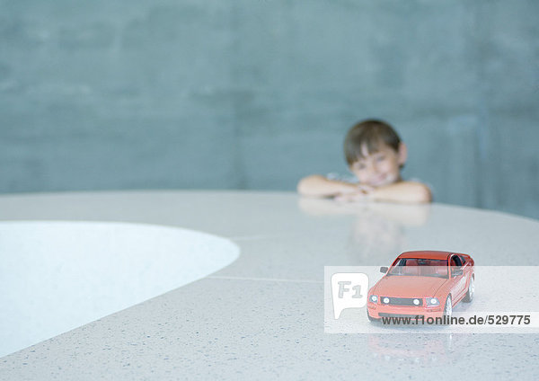 Junge schaut sehnsüchtig auf Spielzeug-Sportwagen
