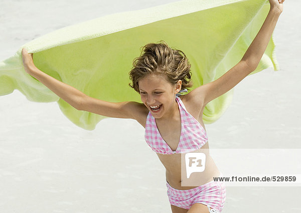 Mädchen hält Handtuch im Wind  am Strand